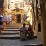 Two people sitting on steps in a narrow, charming street.