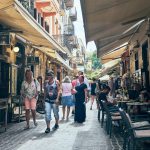 Busy narrow street bustling with people and outdoor cafes.