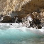 Waves crashing against rocky cliffs by a sea cave.