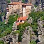 Monastery perched on rocky cliffs surrounded by greenery.