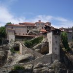 Ancient stone monastery perched atop rocky cliffs under a clear sky.