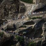 People climbing a winding stone path on a rocky hillside.