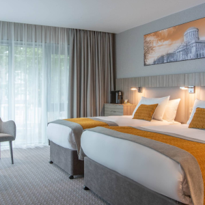 Modern hotel room with twin beds and warm lighting.
