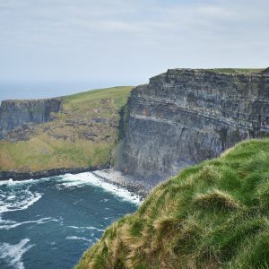 Cliffs overlooking a turbulent sea with green grass on top.