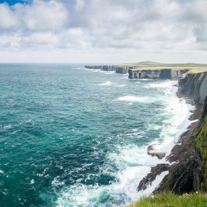 Rugged cliffs overlooking a vast, turbulent sea under a cloudy sky.